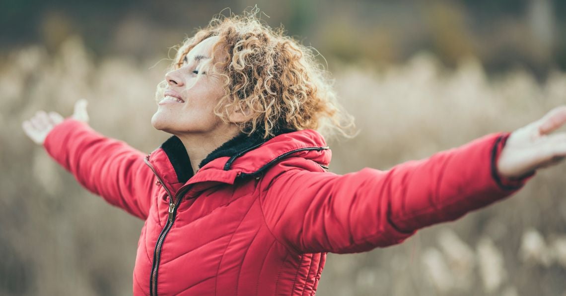 Woman in red coat outside with arms out enjoying nature