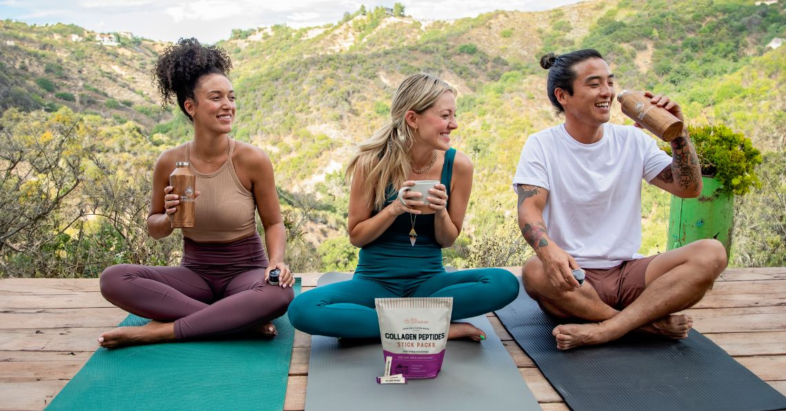 3 people sitting outside on yoga mats laughing and enjoying drinks with a package of Live Conscious Collagen Peptides Stick Packs