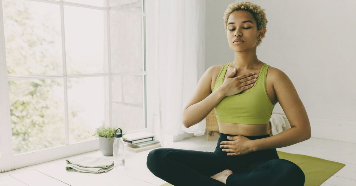 Woman deep breathing on yoga mat with hands on chest and belly