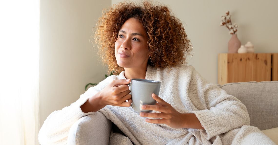 Woman sitting by a window on a couch relaxing with a cup of tea
