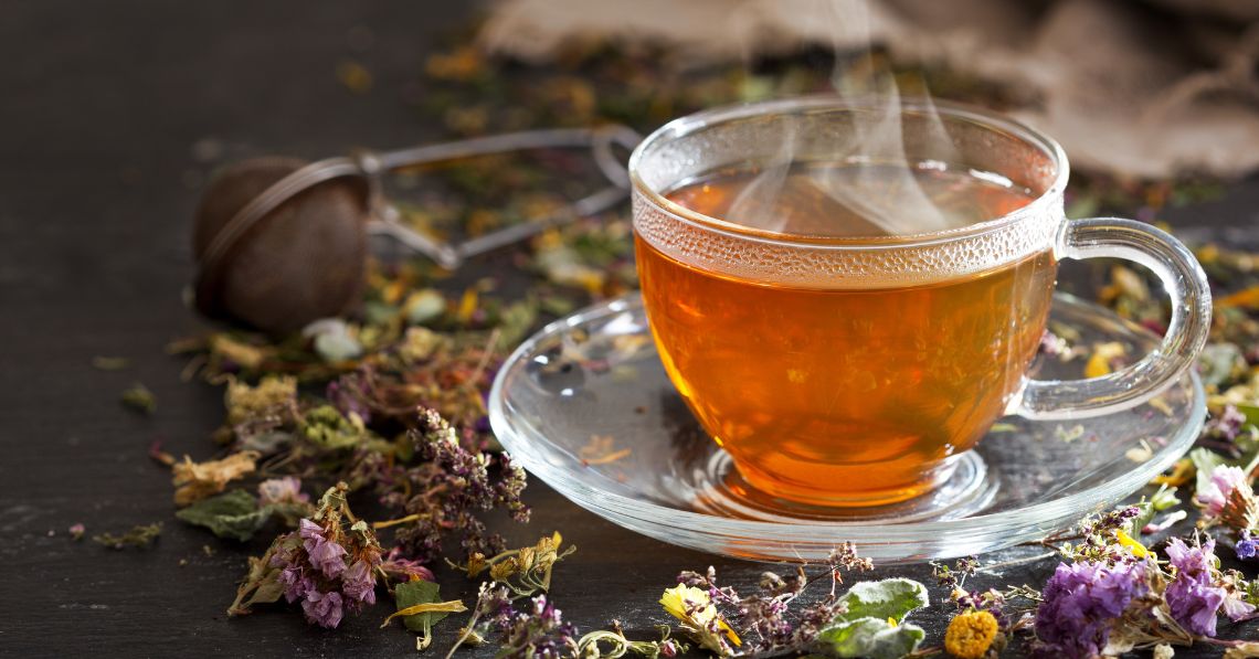 Cup of steaming herbal tea with herbs strewn about