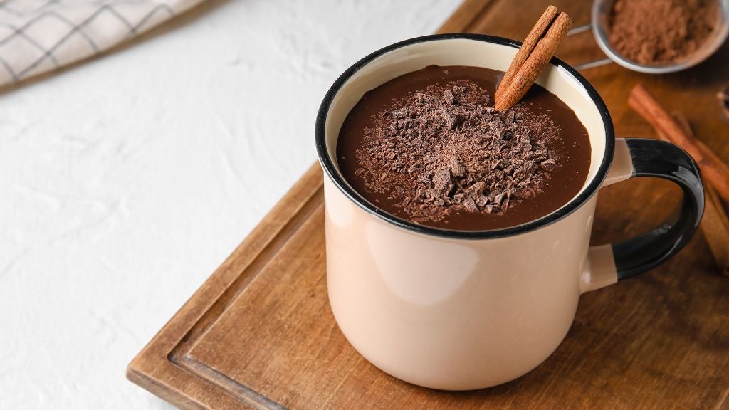 A mug of hot cocoa with a cinnamon stick and crushed chocolate on top