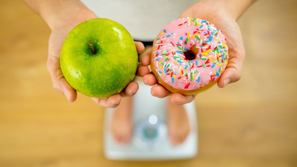 Person standing on scale holding apple and donut