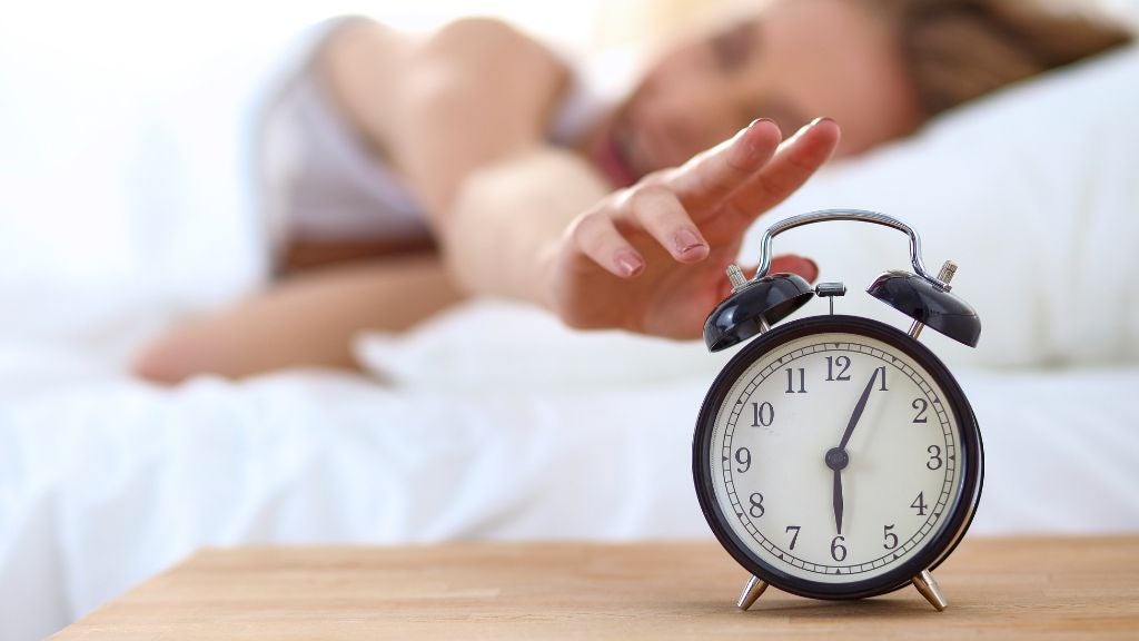 Woman in bed reaching for an alarm clock
