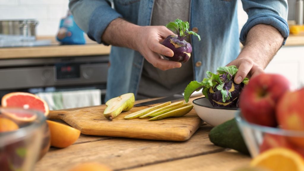 Man with kholrabi and pears on cutting board surrounded by fruit