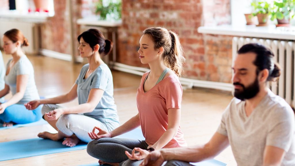 People in a well lighted gym or yoga studio sitting on yoga mats and meditating